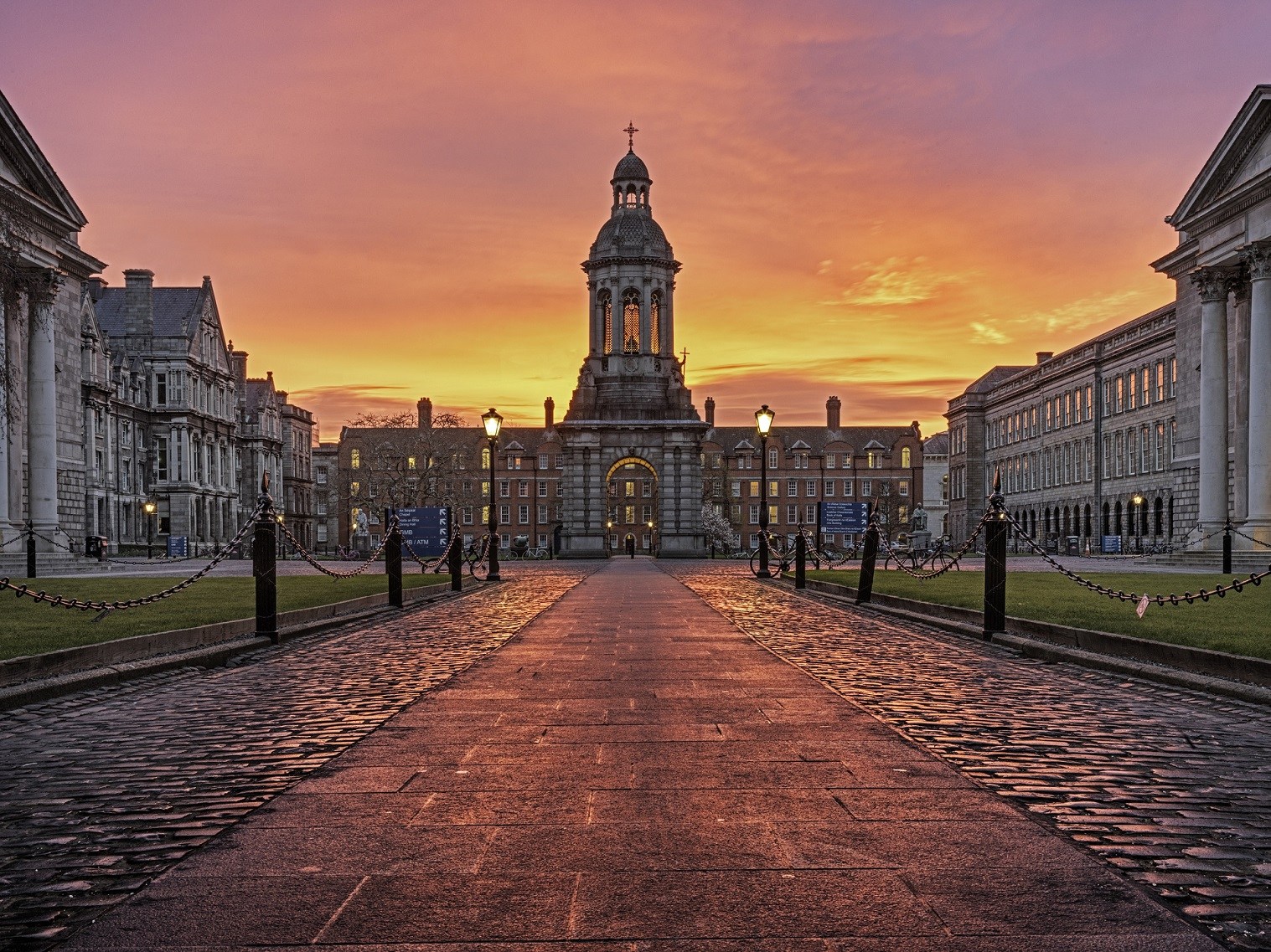 A picture of Trinity College campus with a sunrise backdrop of purple, pink, orange and yellow