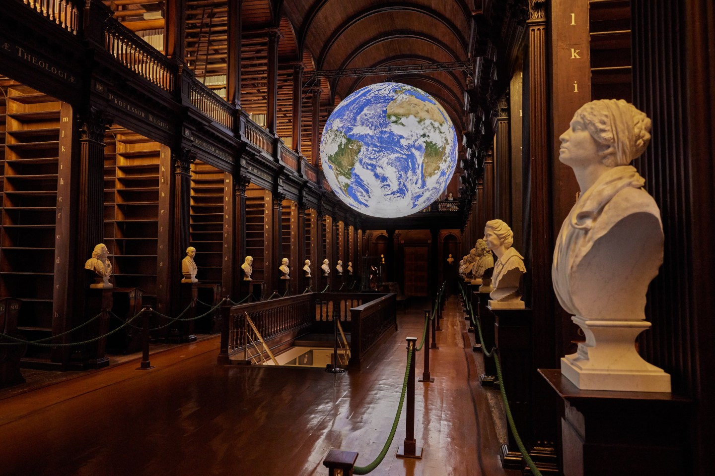 Image of Gaia displayed in the Long Room, with white sculptures along the aisles of bookshelves